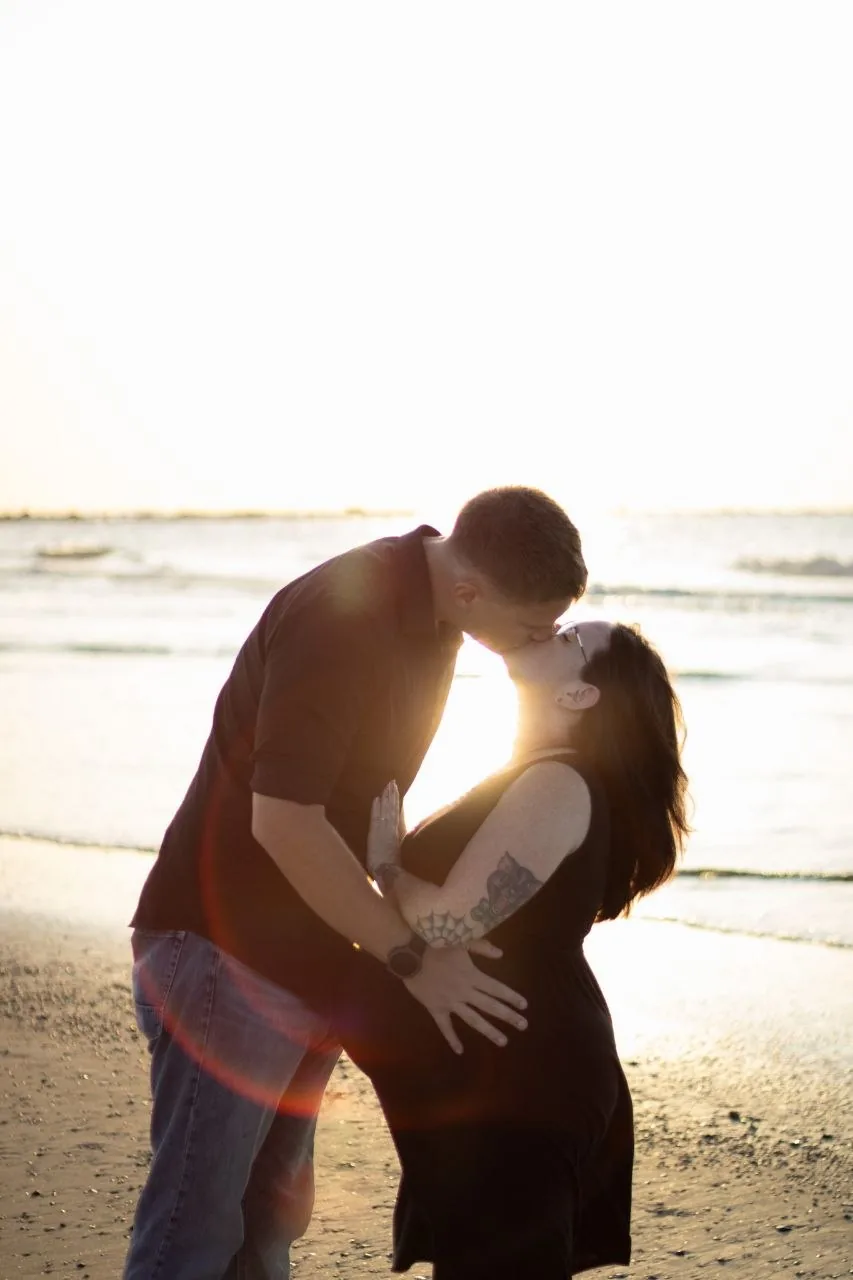 Expecting couple sharing a kiss during a golden-hour beach maternity session.