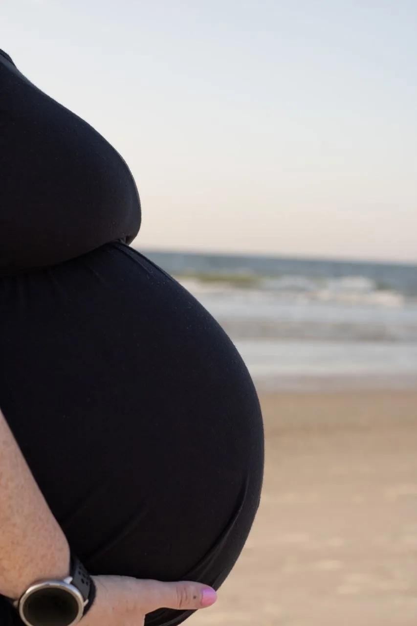 Close-up maternity detail with ocean waves softly blurred in the background.