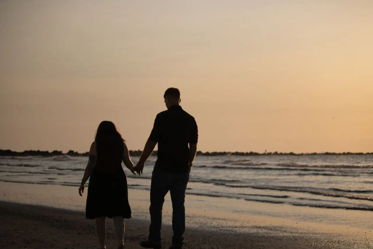 Expecting parents walking hand in hand along the shoreline at sunset.